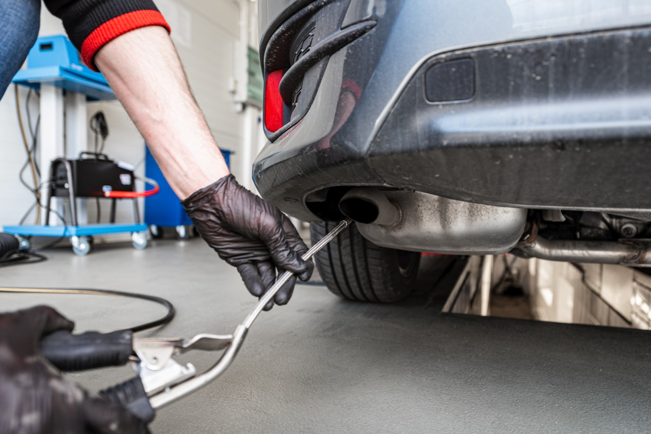 Technician holding an emissions probe at a car exhaust