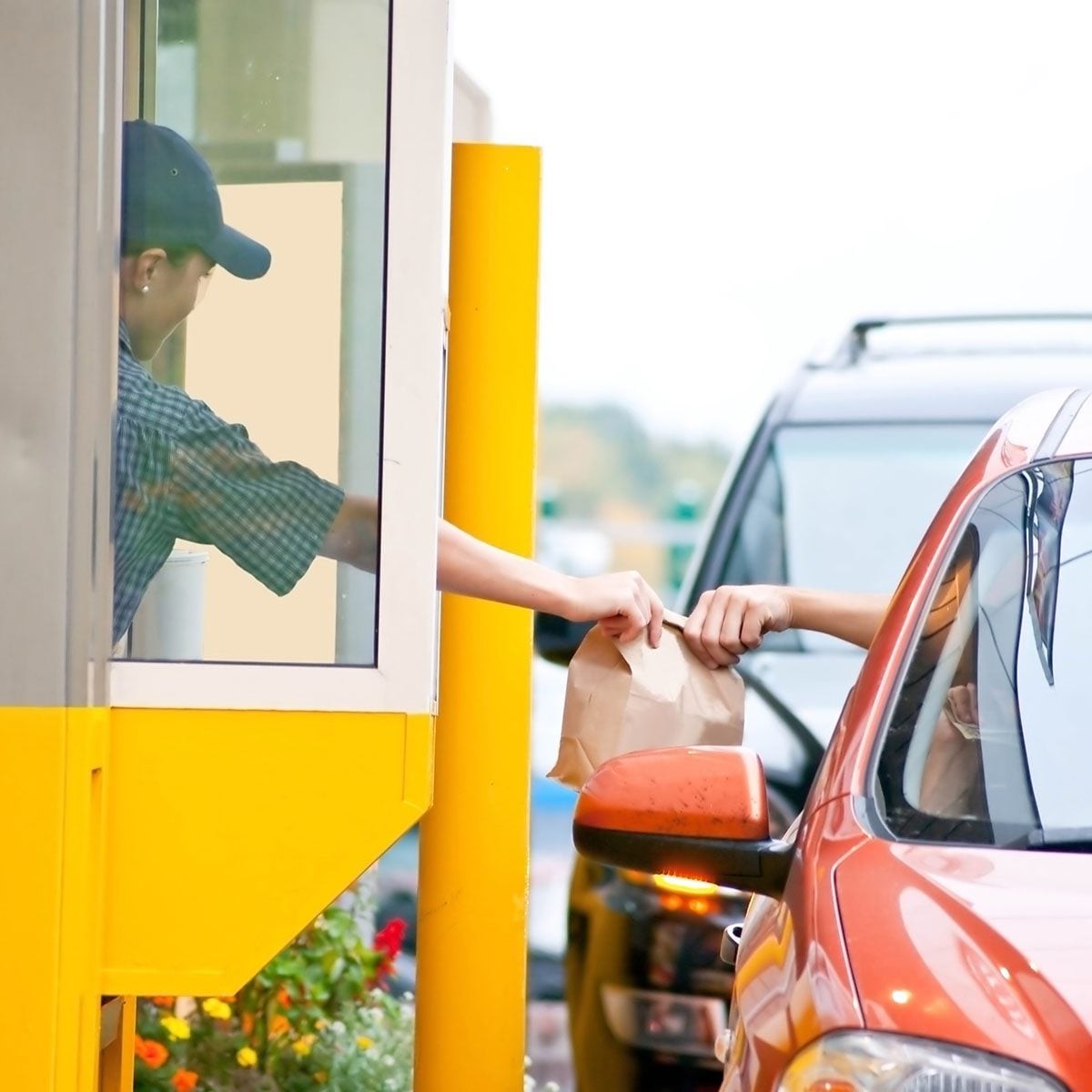 A drive-thru worker handing a paper bag through the serving window to a driver in a waiting car